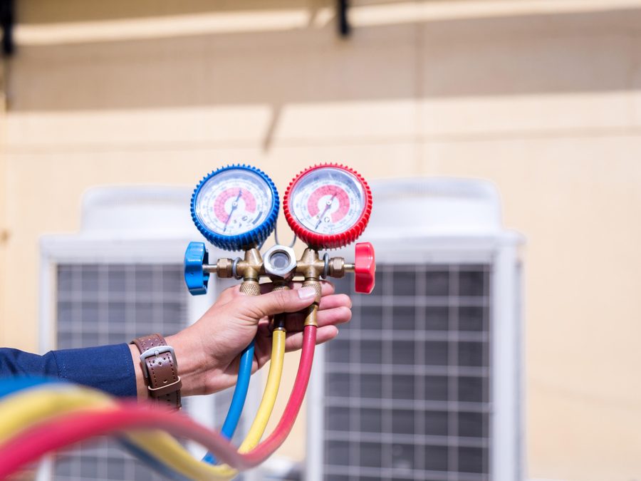 Refrigeration technician checking high and low side pressure gauges during a gas charge