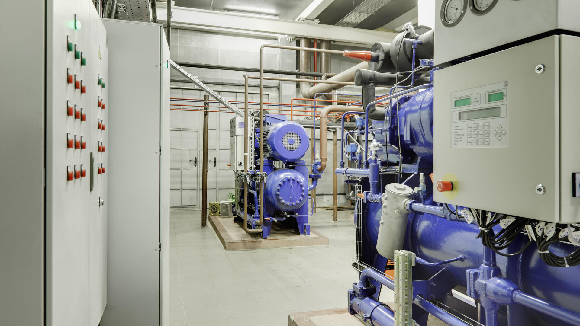 Engineer's view of an industrial chilled-water plant room with control panels and refrigeration machinery