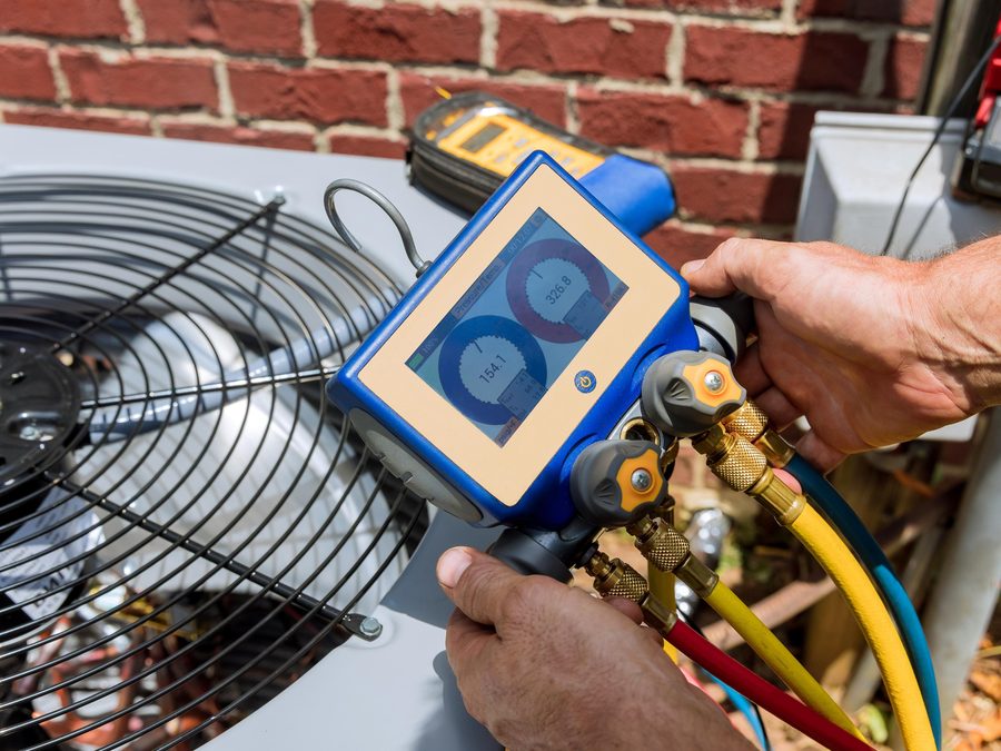 Technician using a digital refrigerant manifold gauge set on an outdoor condensing unit